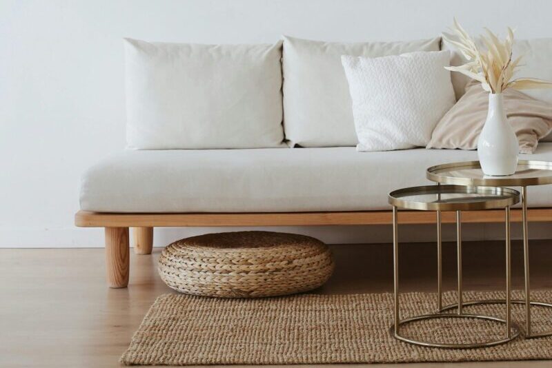 A chic minimalist living room featuring a white sofa with cushions, dried flowers in a vase, and a wooden floor.