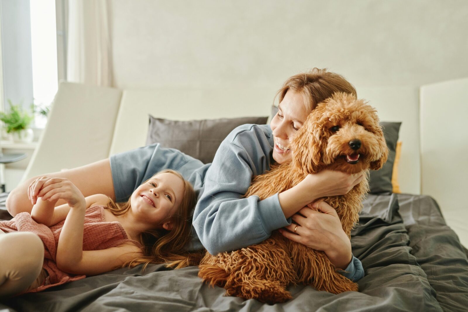 Mother and daughter enjoying quality time with their fluffy pet on a cozy bed.